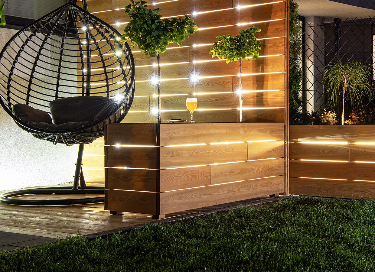 Residential Backyard Garden Wooden Recreation Place Deck with Table Illuminated by LED Outdoor Lighting. Custom Made Wooden Element.